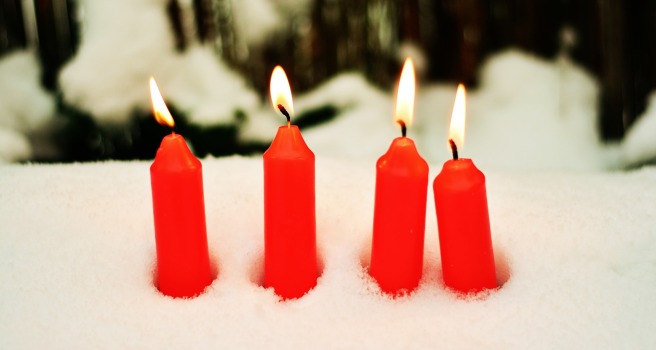 Four red candles burning in a snow bank